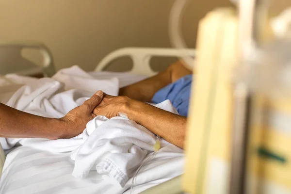Hijo sosteniendo padre es mano en cama en el hospital — Foto de Stock