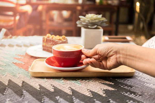 Kvinnlig hand med kopp kaffe och choklad kaka på bordet — Stockfoto
