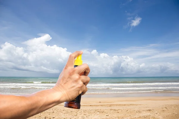 Hand spraying sunscreen protection oil with beach and blue sky