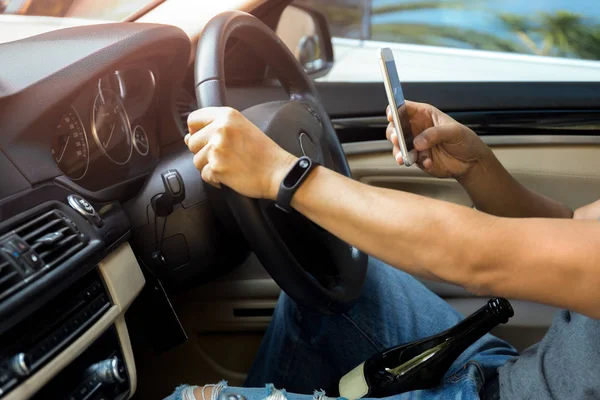 Man met behulp van de telefoon tijdens het rijden de auto met een fles wijn aan hie la — Stockfoto