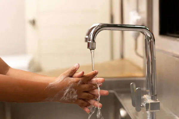 Child washing hands with liquid soap under the tap water