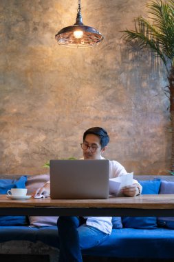 Gözlüklü bir adam laptopunda fatura ödüyor. Kafedeki masada kahve var..