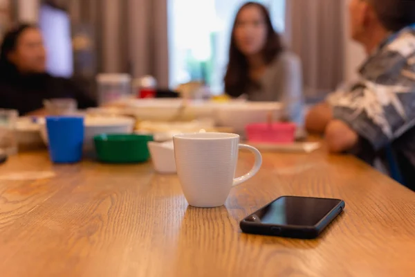 Coffee mug and cell phone on table with beautiful friends having conversation on dinner table.