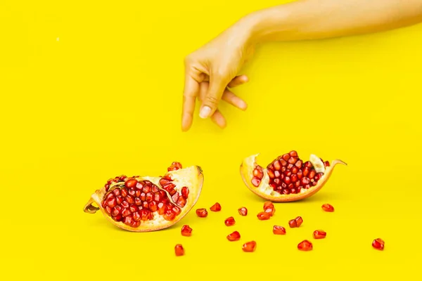 Ripe organic pomegranate fruit with woman hand isolated on yellow background. — Stock Photo, Image
