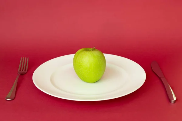 Green on white plate with knife and fork isolated in red background. — Stock Photo, Image