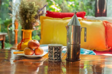 Bir kupa kahve ve elma ahşap masada, renkli kanepe de evde..