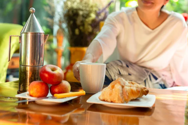 Woman holding mug of coffee with croissants and apple on wooden table. — Stock Photo, Image