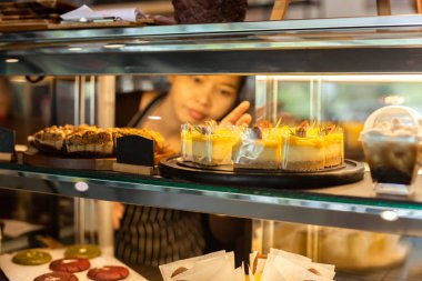 Arka planda garson kızın olduğu bir kafede, vitrinde limonlu kek..