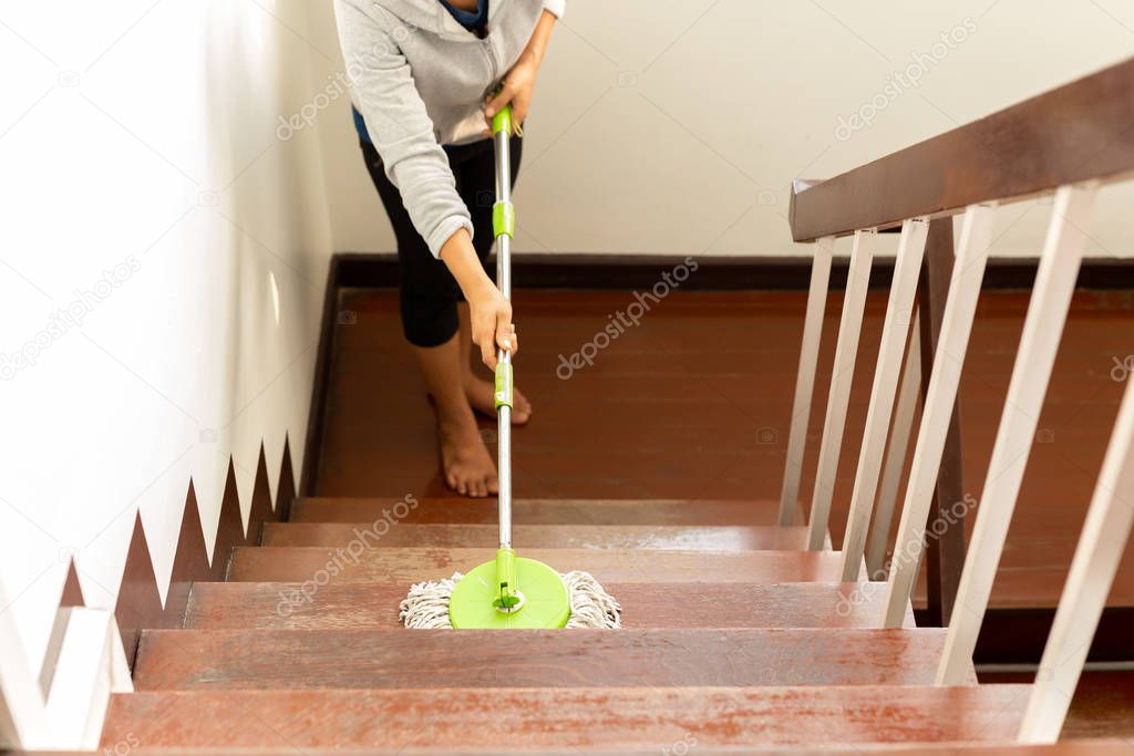 Woman's hand holding a mop cleaning wooden stair.