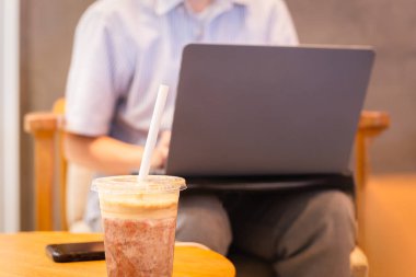 Frappuccino kahvesi kağıt kamışla harmanlanmış ve arka planda dizüstü bilgisayar kullanan bir kadın..