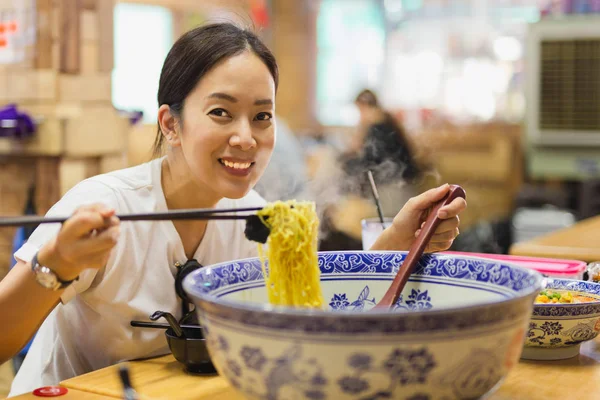 Happy smiling woman eating big bowl of noodle soup in Chinese restaurant. — Stock Photo, Image