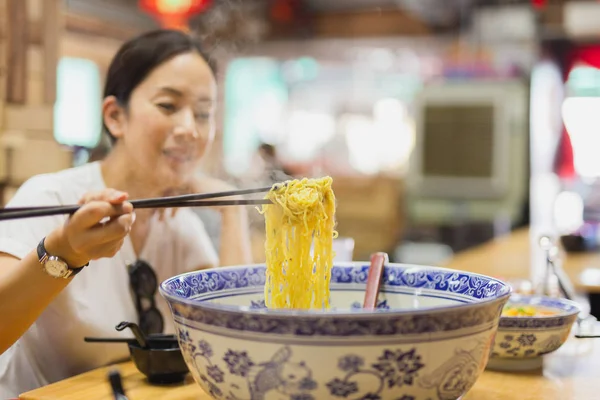 Kvinde spiser nudler suppe i stor skål med spisepinde . - Stock-foto