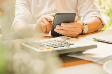 İş adamının elleri ahşap masada hesap makinesiyle akıllı telefonu tutuyor.