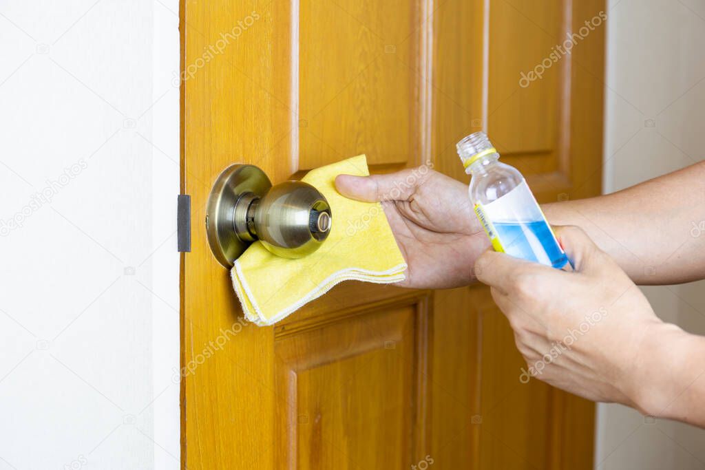 Hand cleaning door knob with alcohol with yellow microfiber cloth. Corona Virus infected protection