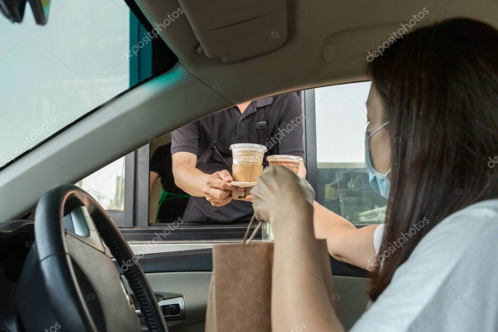 Woman in protective mask taking coffee at drive thru during coronavirus outbreak