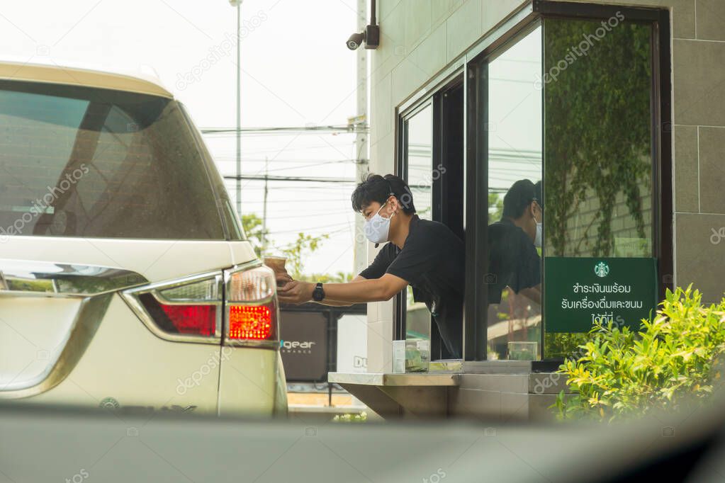 Bangkok Thailand 6 Apr 2020 -  staff with protective mask serving coffee to customer at drive thru counter during coronavirus outbreak