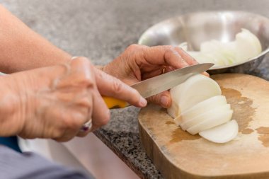 Kıdemli kadın mutfakta tahta bir tahtanın üzerinde soğan doğruyor.