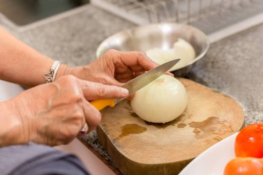 Kıdemli kadın mutfakta tahta bir tahtanın üzerinde soğan doğruyor.