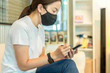 Koruyucu maskeli kadın dijital kalem kullanarak akıllı telefon üzerinde çalışıyor.