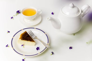 Çay saatinde çay şapkalı ve çaydanlıklı leziz Bask peynirli kek dilimi.