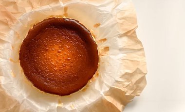 Beyaz arka plandaki fırın kağıdında yanmış Bask peynirli kekinin üst görüntüsü