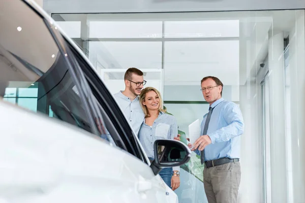 Obchodní Manažer Pomáhá Mladému Páru Vybrat Nové Auto Moderní Autosalonu — Stock fotografie