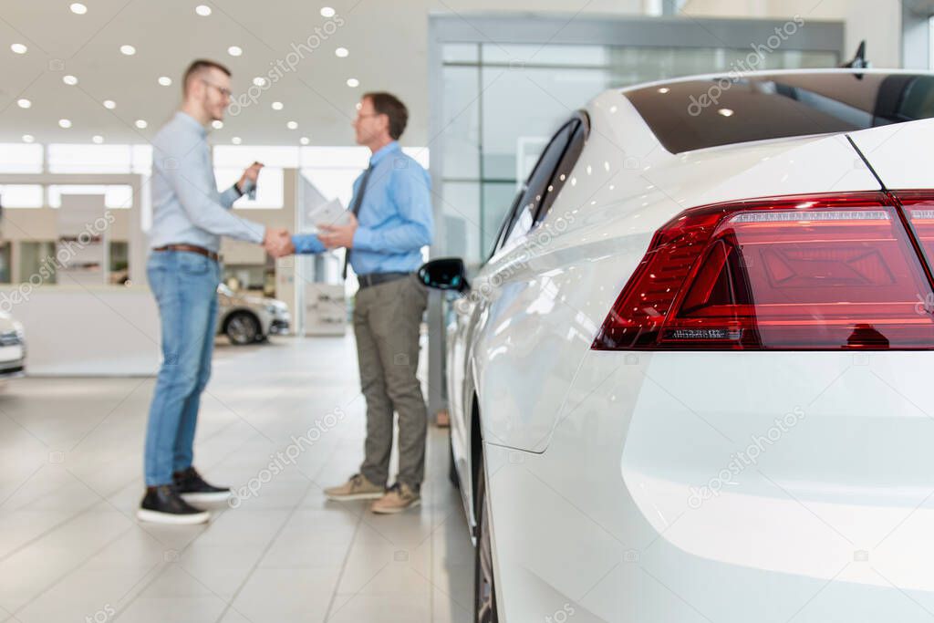 Shaking hands after a successful car buying in modern car showroom. Focus on the vehicle.