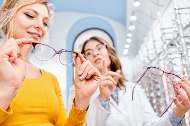 Optisyen bir optik dükkanda gözlük öneriyor ve gösteriyor, reçeteli gözlük için doğru çerçeveyi buluyor