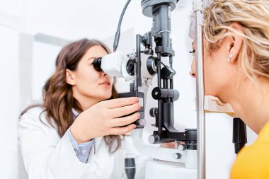 Göz hekimliği kliniğinde doktor ve hasta göz testi yapıyor, görüşü kontrol ediyor.