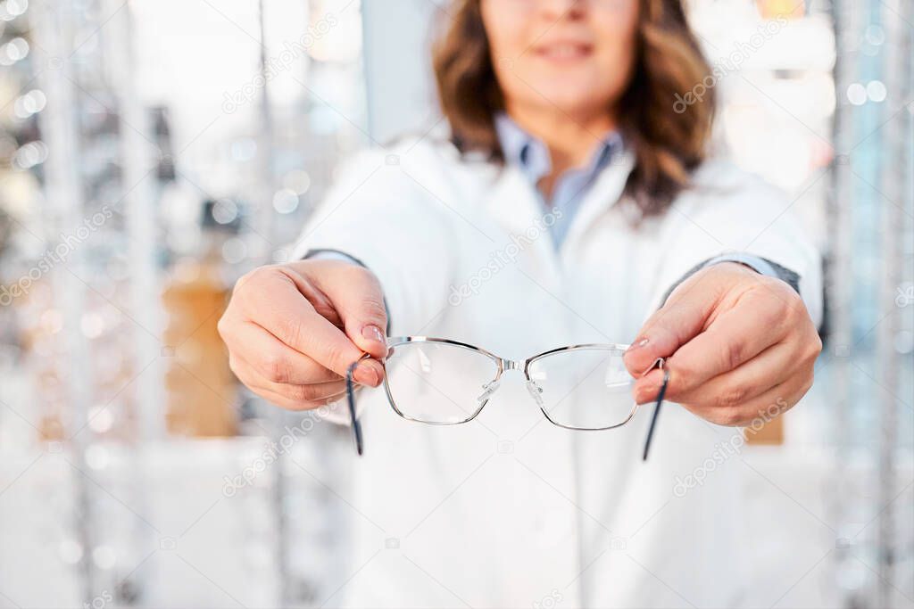 Optician suggesting and showing eyeglasses in an optical shop, finding the right frame for prescription glasses. Focus on glasses