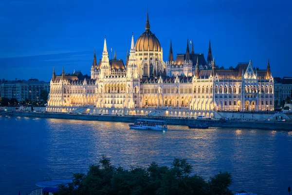 The Budapest Parliament at blue hour. Boats passing by on Danube river, Hungary