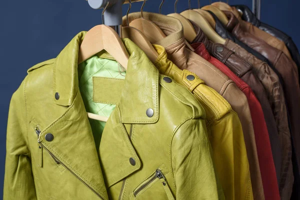 Birçok deri ceket raf üzerinde mavi arka plan asılı renkli