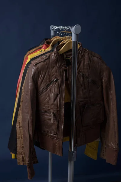 Birçok deri ceket raf üzerinde mavi arka plan asılı renkli