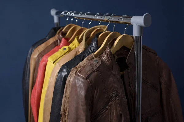 Birçok deri ceket raf üzerinde mavi arka plan asılı renkli