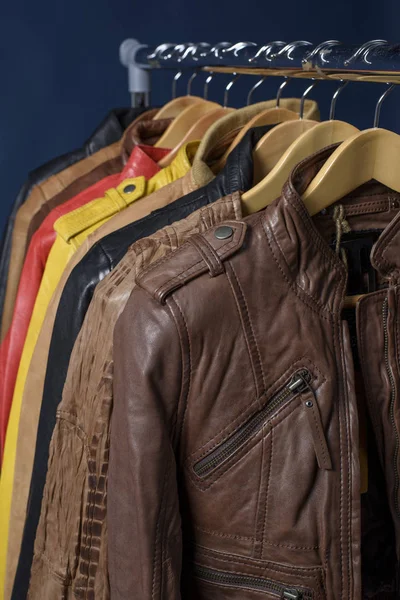 Birçok deri ceket raf üzerinde mavi arka plan asılı renkli