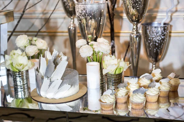 Bolo de casamento e cupcakes na mesa decorados com flores brancas e velas e vasos — Fotografia de Stock