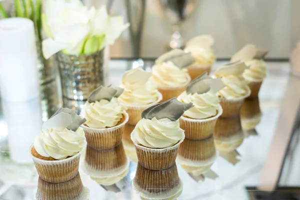 Cupcakes com creme branco na mesa decorado com flores brancas e velas — Fotografia de Stock