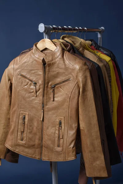 Birçok deri ceket raf üzerinde mavi arka plan asılı renkli