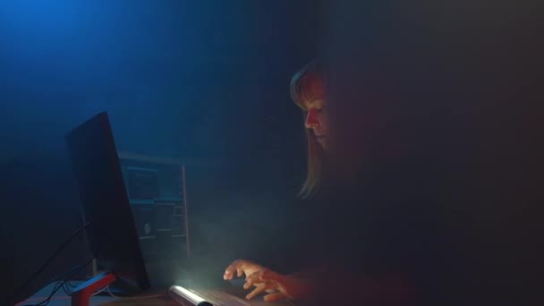 Hacker-Programmiererin arbeitet an einem Computer in einem unterirdischen Büro, das mit Bildschirmen und Rauch gefüllt ist. Blaues Neonlicht erhellt den Raum. Digitale Freiheit. — Stockvideo