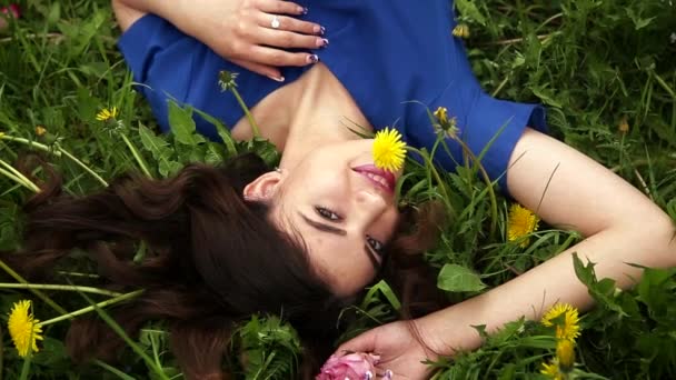 Attractive fashionable girl is lying on the grass and enjoying a beautiful summer day in the blooming forest — Stock Video
