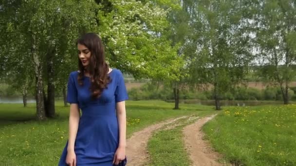 Hübsche Frau mit langen Haaren im blauen Kleid spaziert durch den blühenden Garten. — Stockvideo