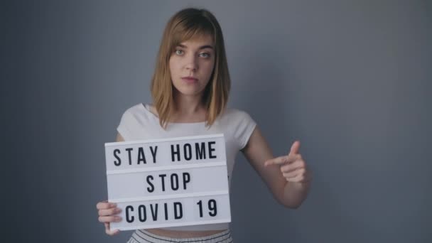 Fiatal lány áll egy táblával, hogy "Maradj otthon stop covid-19" — Stock videók