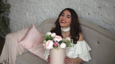Uzun siyah saçlı çekici bir kadın sunulan çiçek buketiyle çok hoş. Beyaz elbise giyiyor..