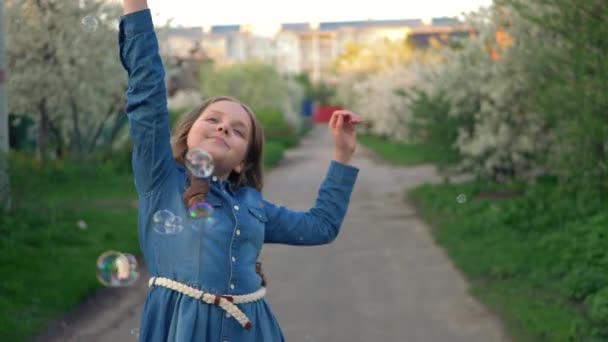 Malá roztomilá dívka chytí bubliny na jasně kvetoucí ulici. — Stock video