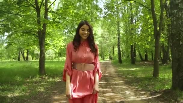 Bella donna alla moda con i capelli lunghi in abito rosa sta camminando nella foresta in fiore — Video Stock