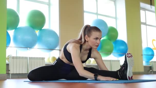 Αθλητικό ελκυστικό λεπτό κορίτσι με μακριά μαλλιά τεντώνεται σε λαστιχένιο χαλί στο γυμναστήριο του αθλητισμού. — Αρχείο Βίντεο