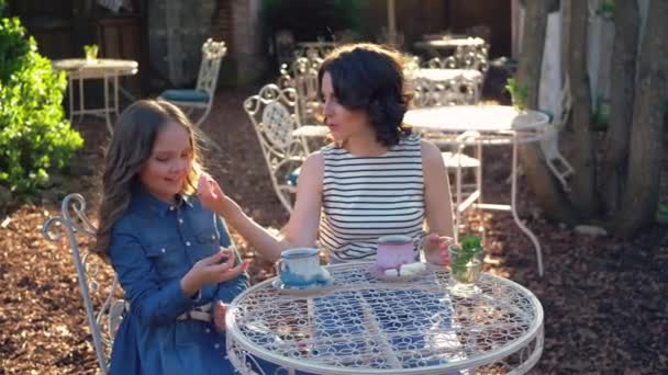 妈妈和她可爱的小女儿在公园里玩的开心 她带着老式餐桌和两杯茶 妈妈一边和女儿玩耍 一边慢吞吞地吃棉花糖 他们很开心 — 图库视频影像