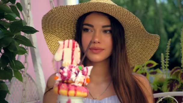 戴着宽边帽的迷人女人正在喝甜奶昔和多层甜点 — 图库视频影像