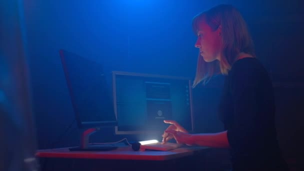 魅力的な女性ハッカープログラマーは暗い地下のオフィスルームでコンピュータに取り組んでいます 青いネオンが部屋を満たしています 彼女はログイン情報を盗むためにソフトウェアに入る — ストック動画