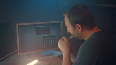Siber terörist sigara içiyor ve karanlık ofis odasında bilgisayar üzerinde çalışıyor. Erkek hacker masada iki monitörle oturuyor. Program kodu gösteriliyor. Güvenlik sistemini başarıyla hackliyor..